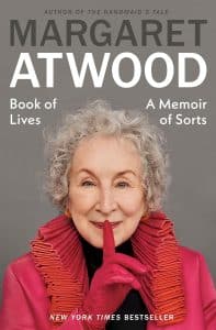 Book cover of Book of Lives: A Memoir of Sorts by Margaret Atwood showing her making a shhh sign with her finger over her smiling lips.